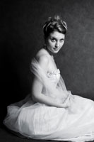 Художественный фотопортрет девушки в бальном платье, сидящей на студийном фоне