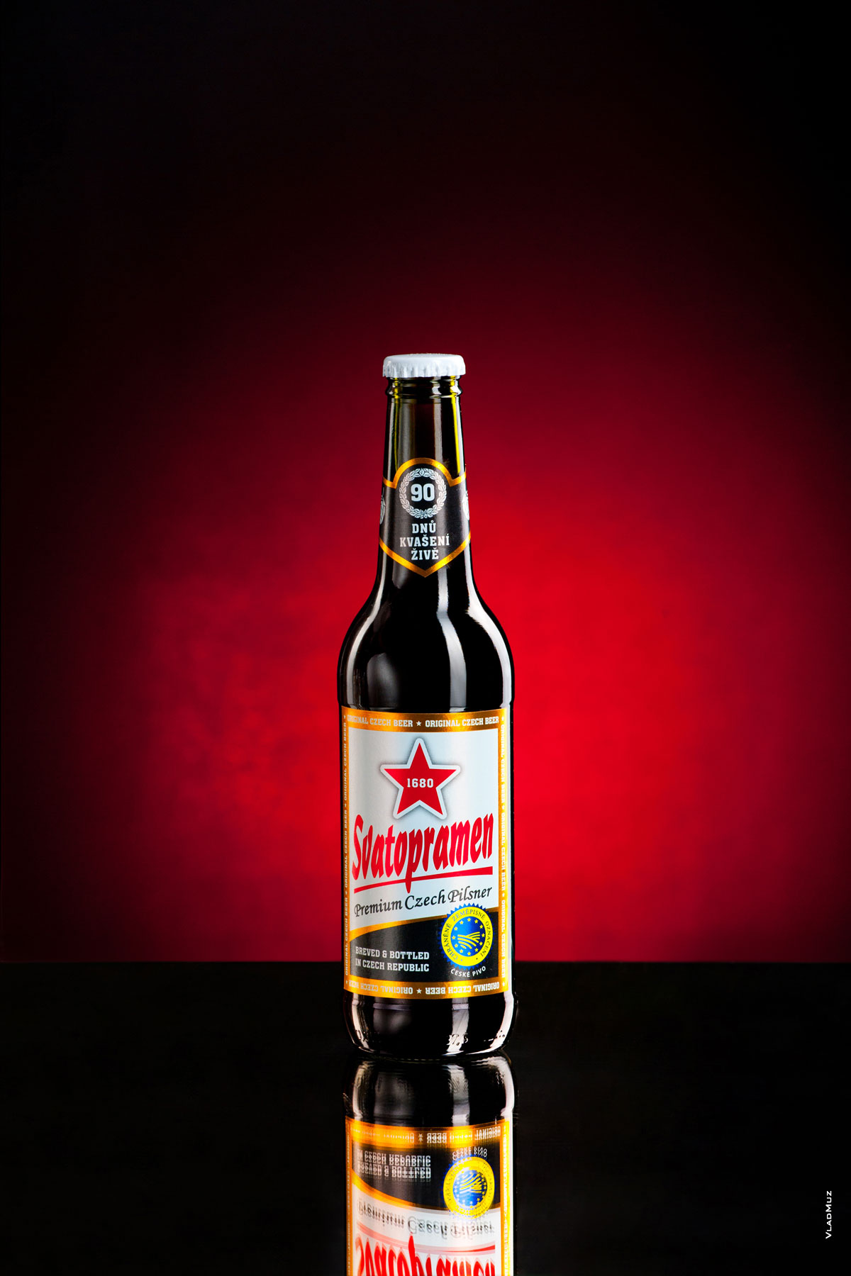 Фото пивной бутылки с темным лежаком «Святопрамен» на темно-красном фоне