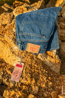 Фото синих джинсов с патчем на поясе и бумажным ярлыком с логотипом Woodcutter на фоне желтого ракушечника