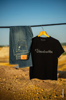 Фото синих джинсов и черной футболки с логотипом Woodcutter, висящих на перекладине, на фоне карьера