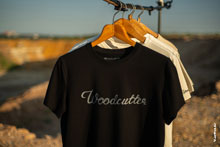 Фото черной футболки с логотипом Woodcutter на вешалке на фоне карьера