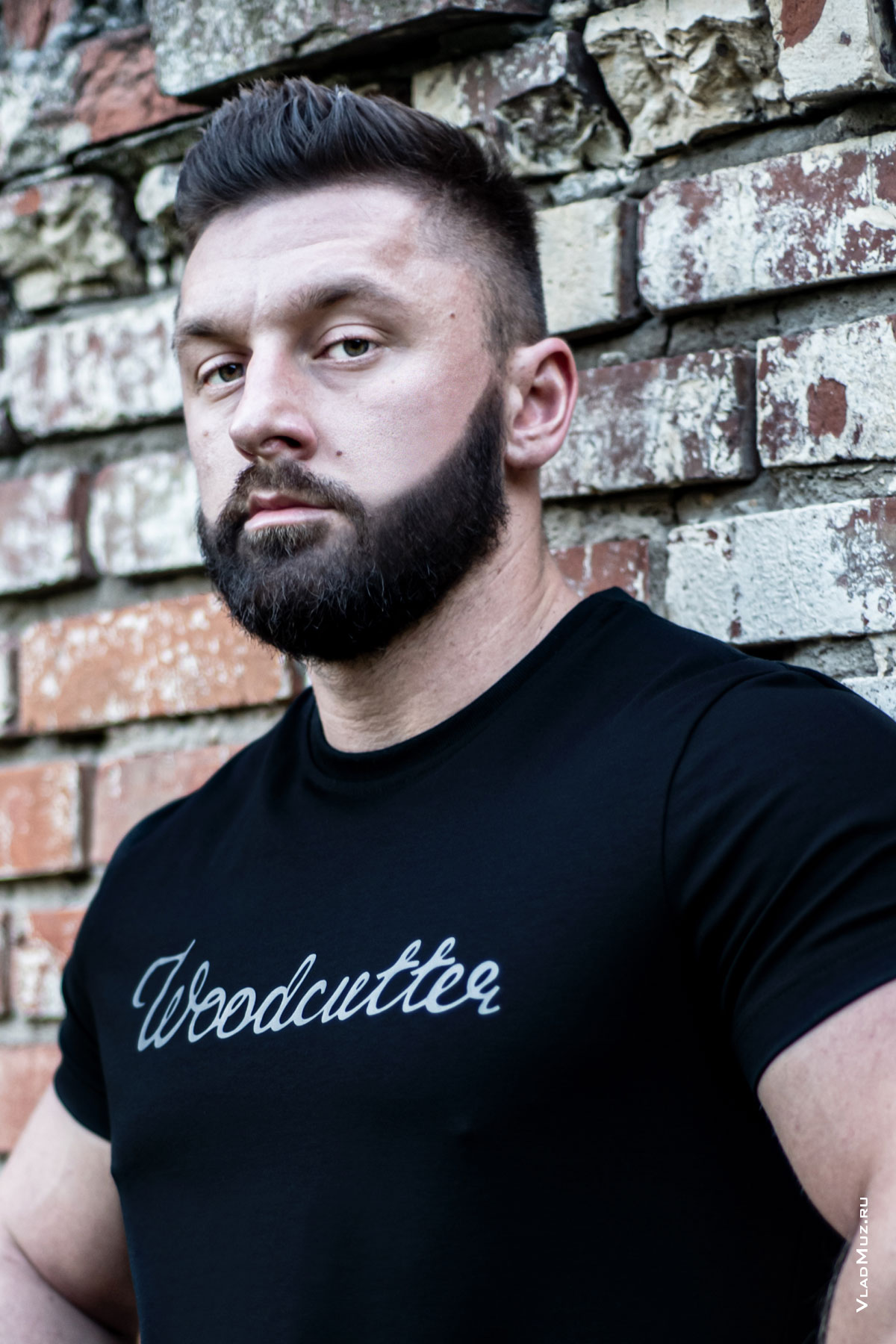 Грудной рекламный фотопортрет мужчины у кирпичной стены в черной футболке Woodcutter