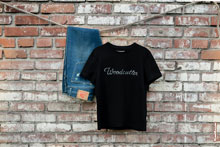 Фото синих джинсов и черной футболки Woodcutter на фоне кирпичной стены