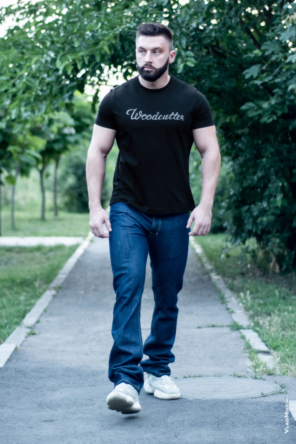 Фото в полный рост идущего по тротуару мужчины в джинсах и черной футболке Woodcutter