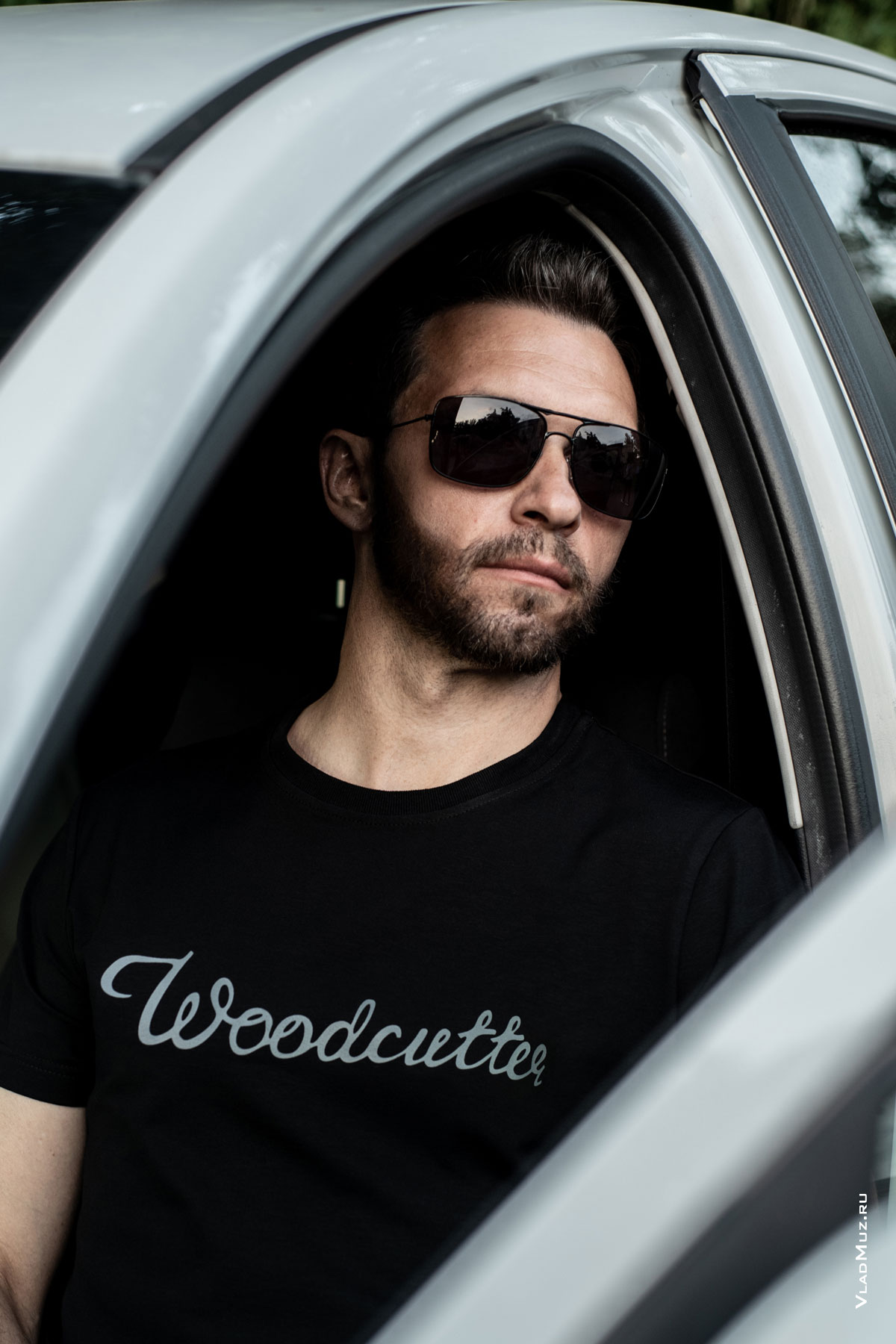 Рекламный фотопортрет мужчины в черной футболке с брендом Woodcutter, сидя в автомобиле
