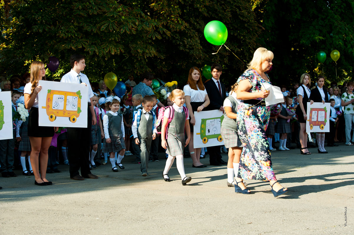 Фото учителя и первоклассников, идущих к парадному входу для выступления перед школой