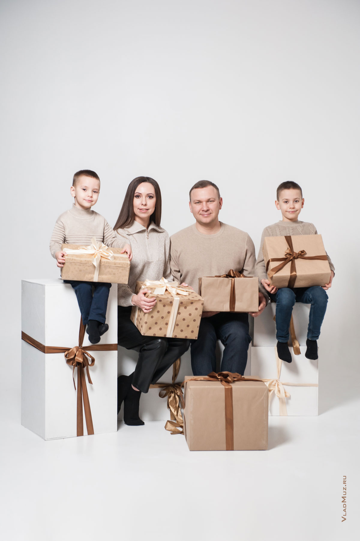 Вертикальное семейное фото родителей с детьми, с подарками в руках, на белом фоне в студии
