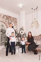Семейное фото родителей с 2-мя детьми в белой студии на фоне новогодних ёлок