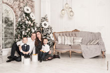 Весёлое эмоциональное семейное фото в студии с 2-мя детьми на фоне новогодних ёлок