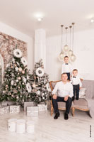Фото папы с 2-мя маленькими детьми в светлой студии на фоне новогодних елок