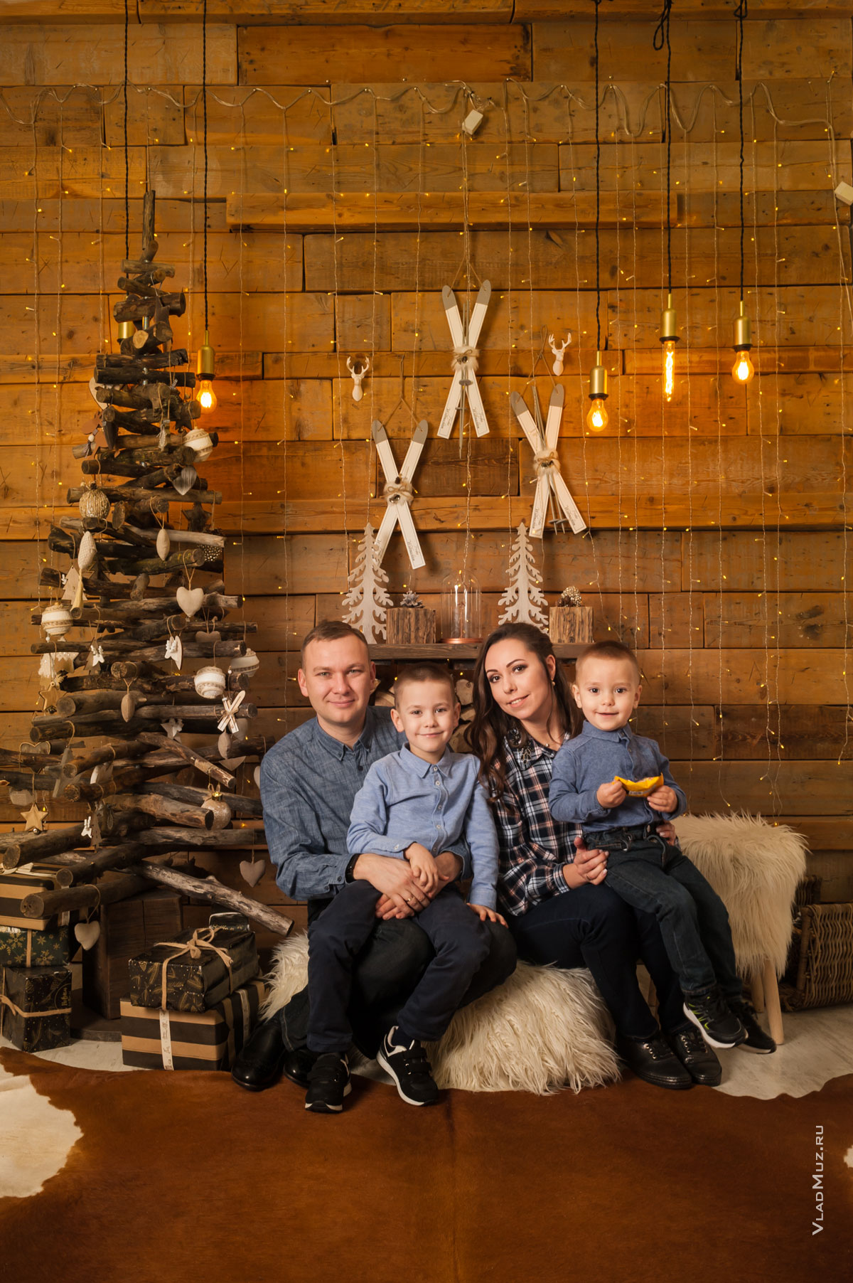 Новогодний семейный фотопортрет с 2-мя детьми на фоне деревянной стены и стилизованной деревянной ёлки