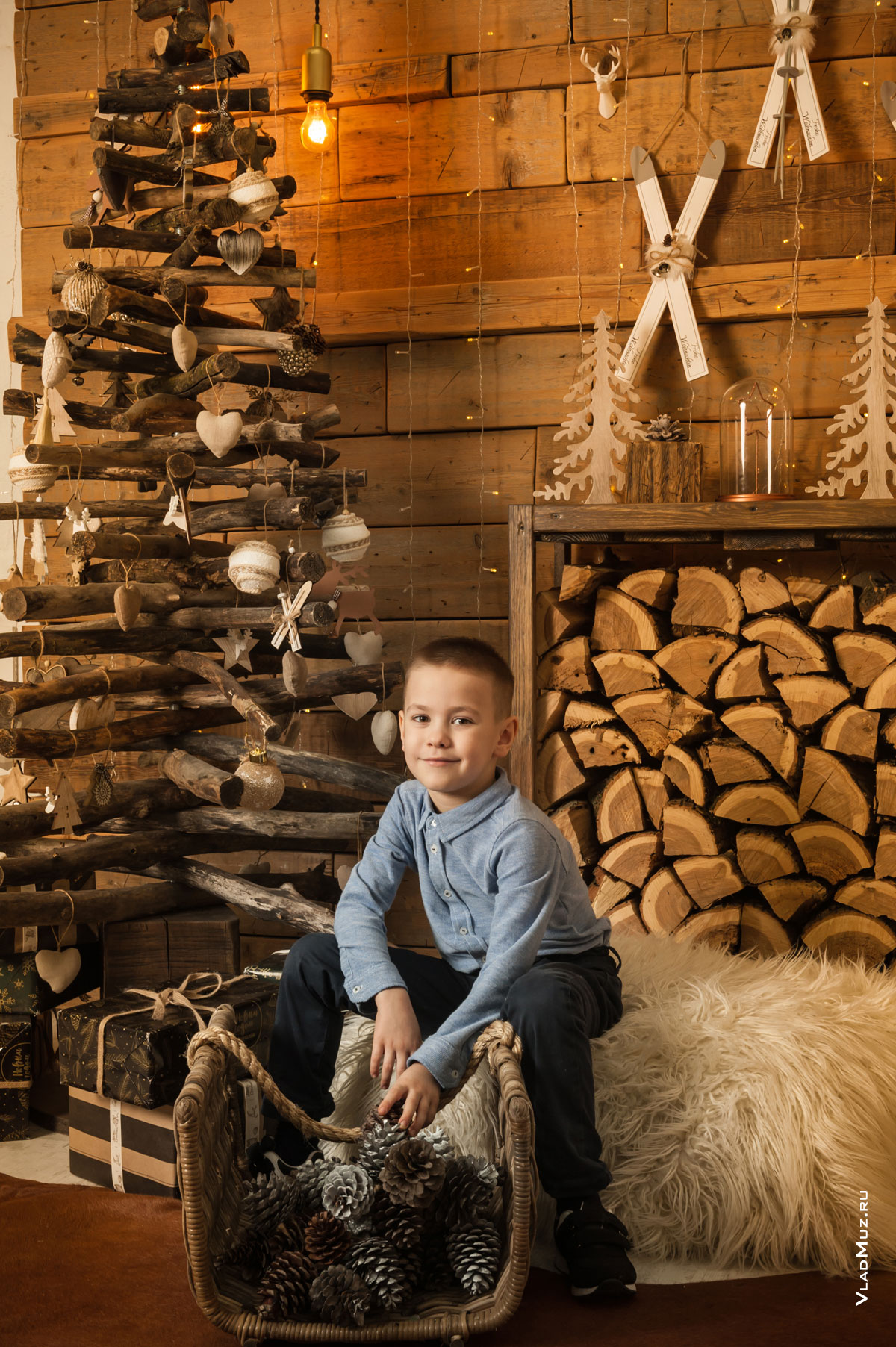 Новогоднее фото мальчика в студии на фоне деревянной стены, деревянной елки и других декораций из дерева