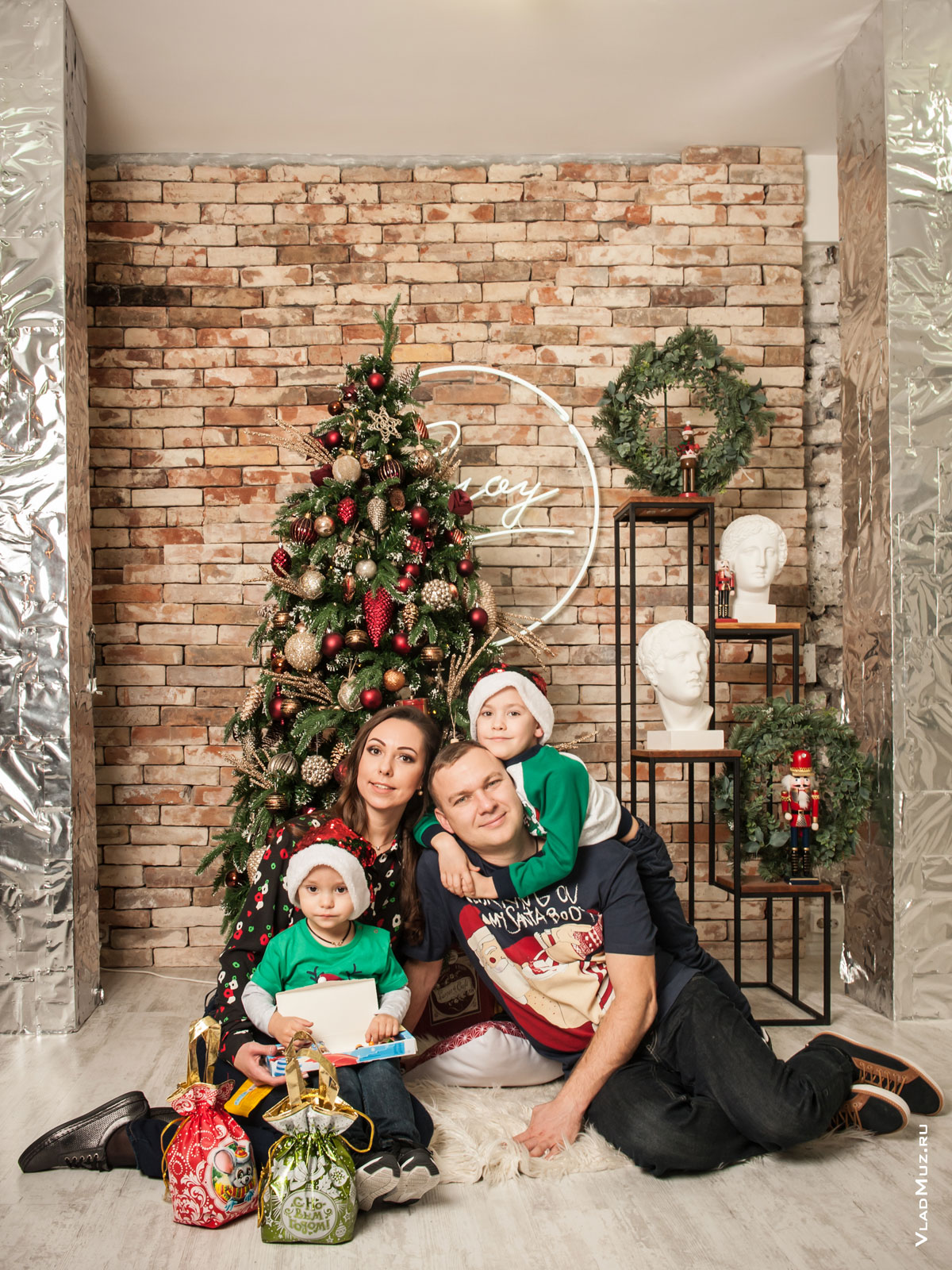 Фото семейной пары с маленькими детьми в студии на фоне елки и новогодних декораций