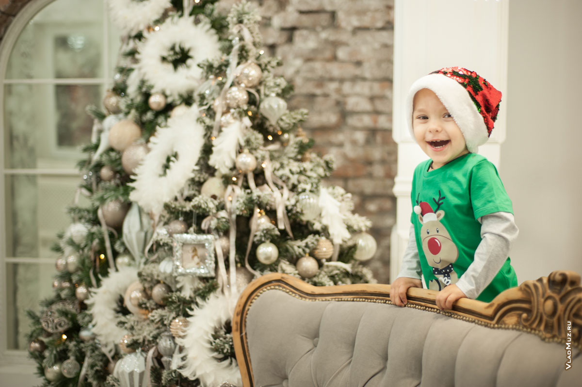 Фото малыша в студии в новогодней шапке-колпаке на фоне ёлки