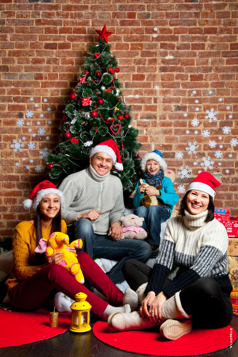 Веселый семейный квартет в новогодних шапках-колпаках на фоне праздничной елки