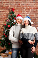 Теплое семейное фото в вязанных свитерах и новогодних шапках на фоне елки