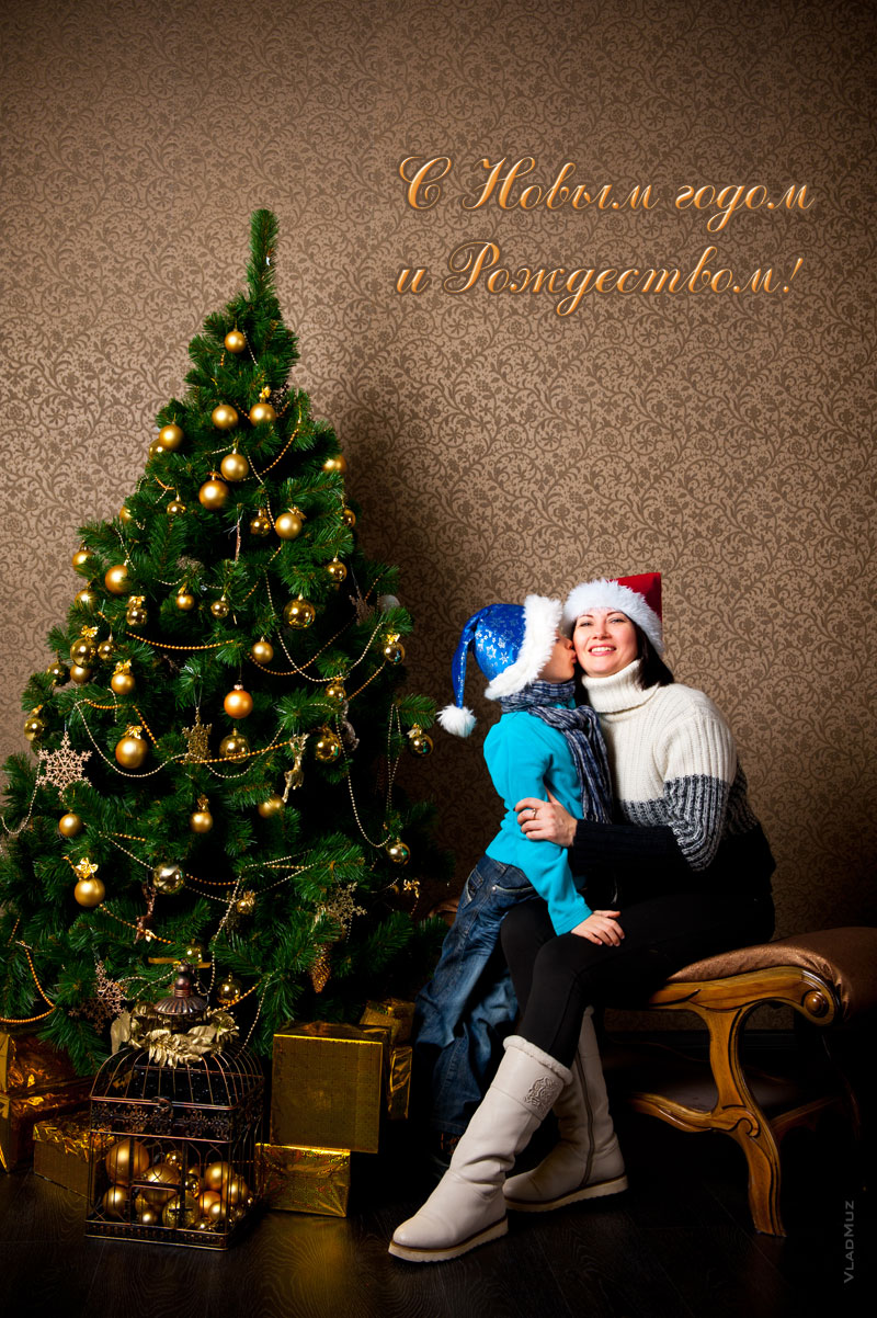 Новогоднее фото поцелуя мамы с сыном рядом с наряженной елкой, с надписью «С Новым годом и Рождеством!»