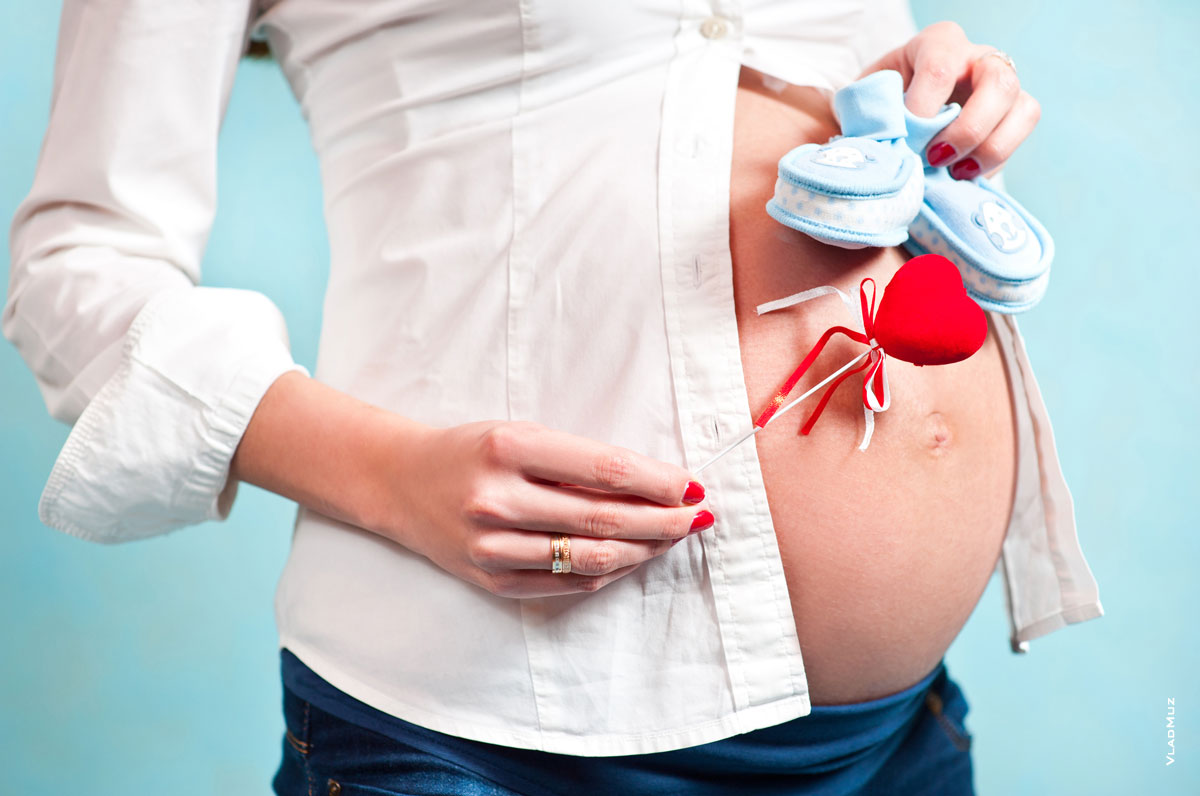 Фото живота беременной девушки, красного сердца и голубых пинеток