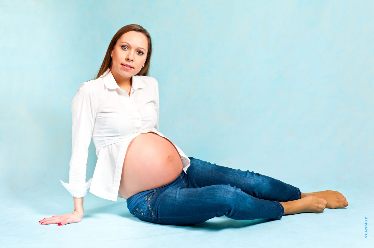 Фото беременной девушки на студийном голубом фоне сидя