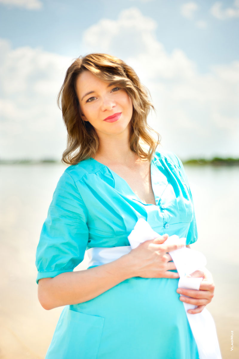 Поясной фотопортрет беременной девушки в светлых тонах с руками на животе
