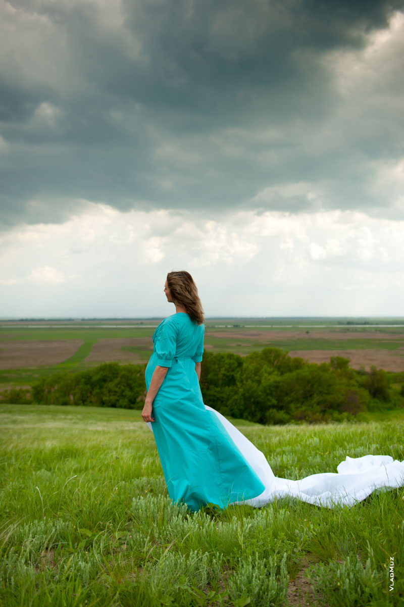 Фото девушки в платье на холме, со спины, на фоне грозового неба