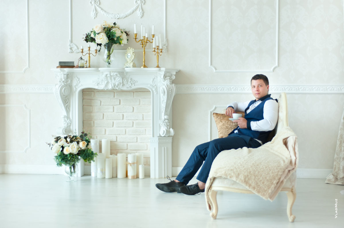 Фотография будущего папы в студии у камина, сидя на диване-кушетке с кофе