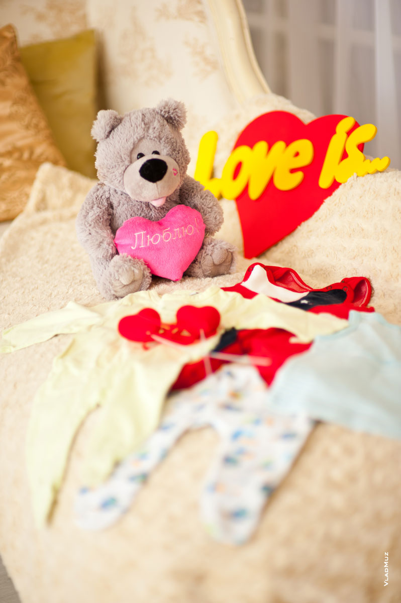 Фотонатюрморт: детская одежда, мягкая игрушка медвежонка и буквы “Love is”