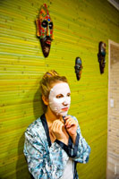 Жанровый фотопортрет девушки в косметической маске на фоне коллекции деревянных масок