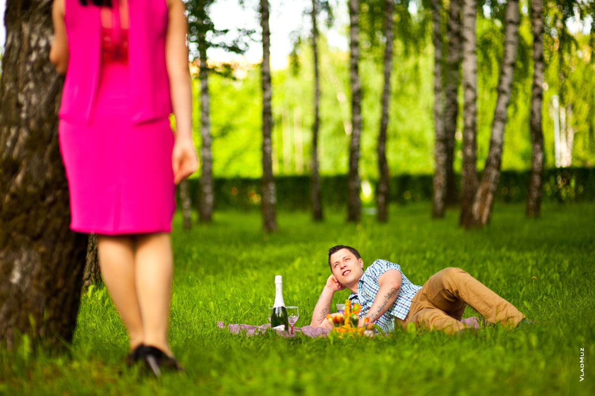 Фото девушки, стоящей у дерева, юноша, лежа на лужайке, смотрит на нее