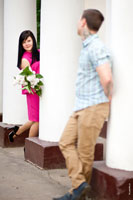 Игровой момент фотосессии: мужчина стоит у белой колонны, девушка с букетом выглядывает из-за колонны рядом