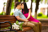 Фото сирени на скамейке в фокусе на переднем плане, вдали сидит влюбленная пара в расфокусе