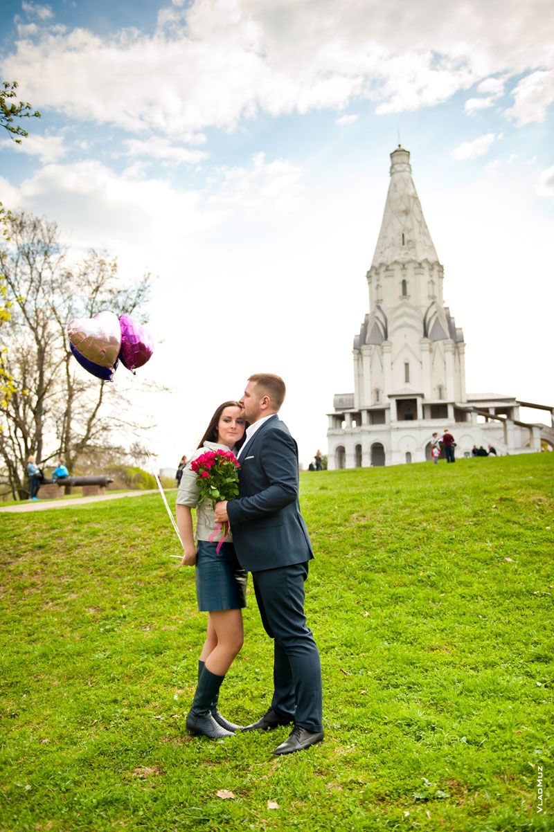 Впереди - мужчина с букетом и девушка с воздушными шарами, вдали - храм Вознесения Господня