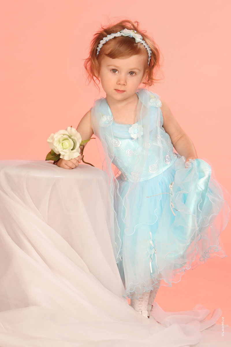 Студийное фото девочки-модели в платье в полный рост с цветком в руках