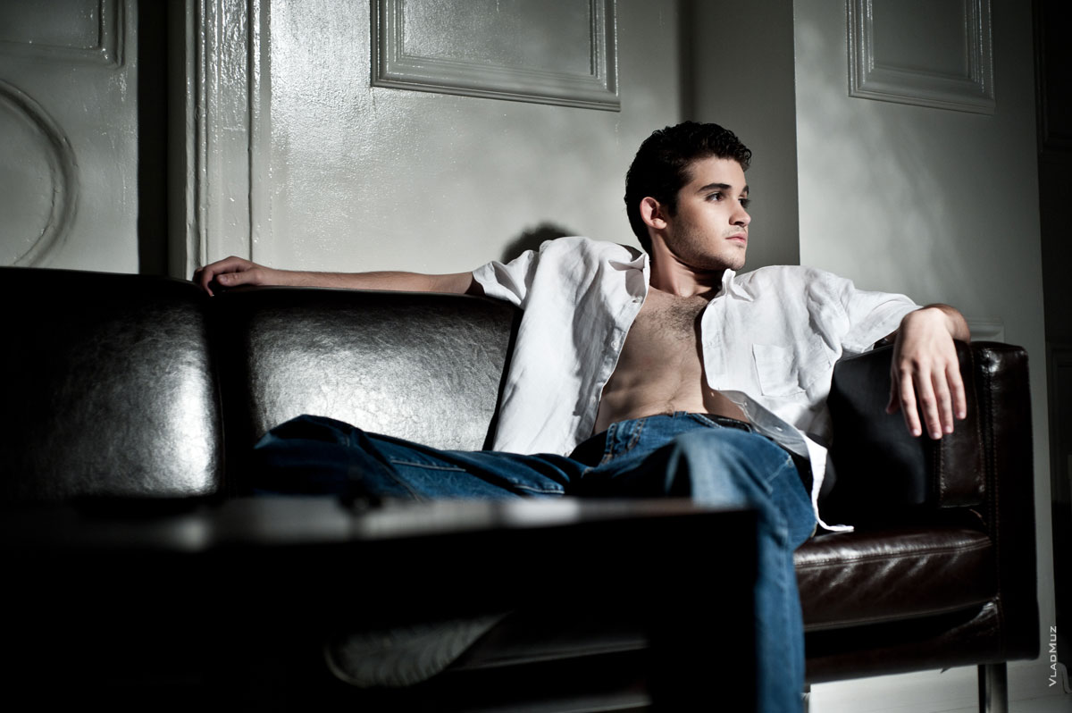 Фото мужчины в расстегнутой рубашке и джинсах, сидя на диване в расслабленной позе