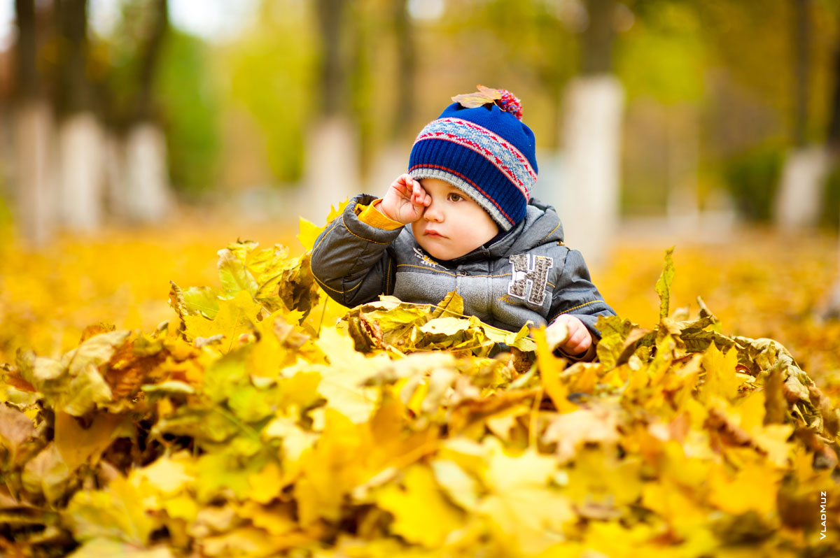 Осеннее фото ребенка в парке, с рукой у лица, на ковре из опавших осенних листьев