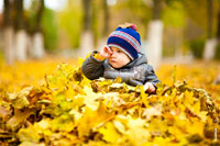 Осеннее фото ребенка в парке, с рукой у лица, на ковре из опавших осенних листьев