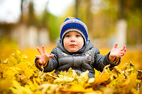 Осеннее фото ребенка, с расставленными перед собой руками, сидя на желтых листьях
