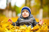 Осеннее фото ребенка в парке на желтых листьях, смотрящего вверх, с расставленными перед собой руками