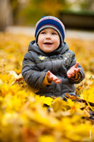 Детский осенний фотопортрет смеющегося мальчика, сидящего на желтой листве