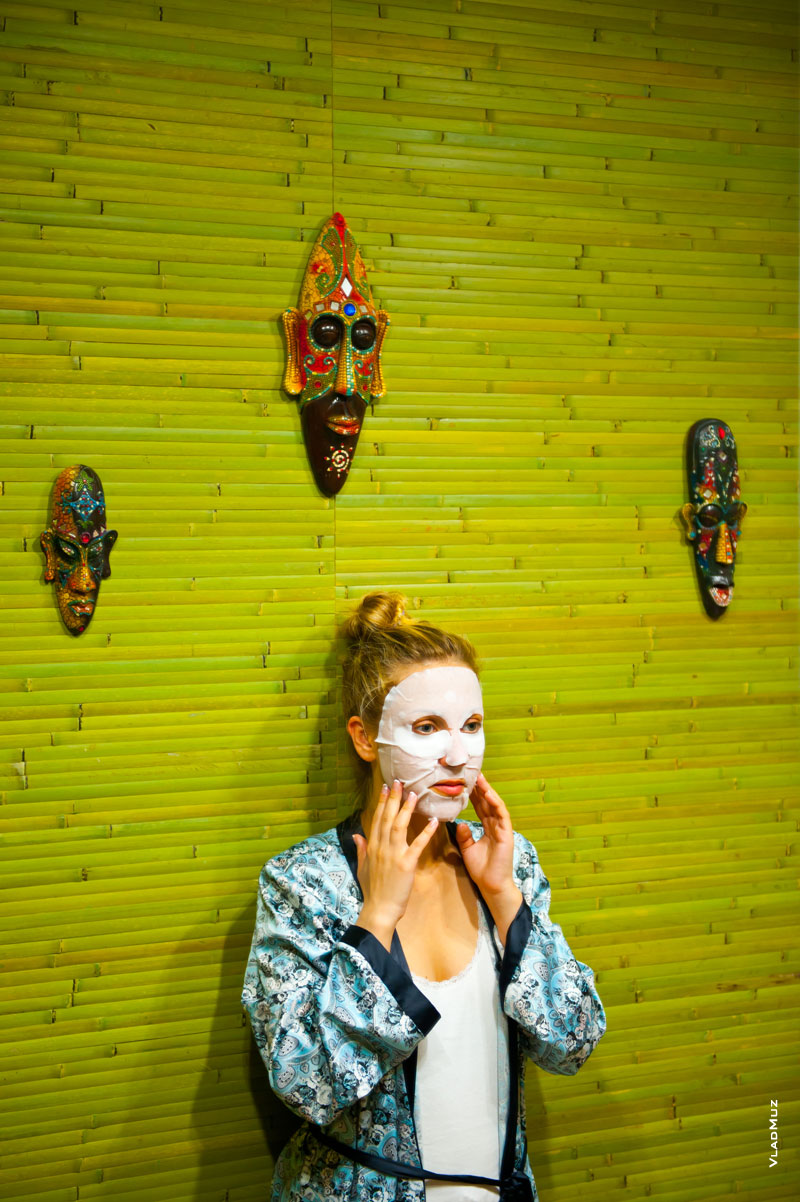 Жанровый фотопортрет невесты в косметической маске перед свадьбой на фоне коллекции деревянных масок