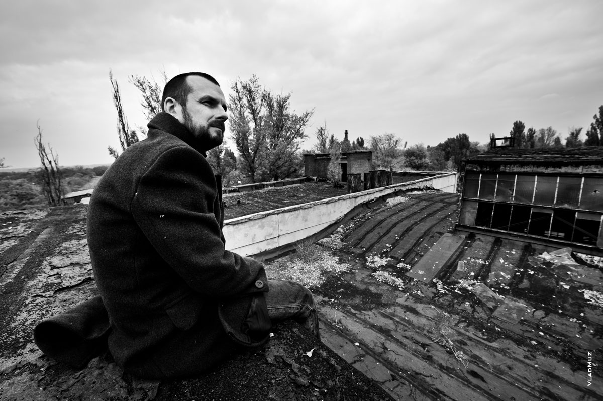 Жанровый портрет мужчины в пальто, сидящего на краю крыши