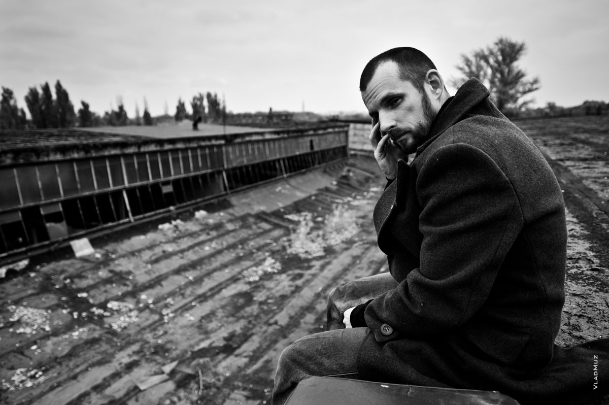 Черно-белый портрет мужчины в пальто, сидящего на краю крыши