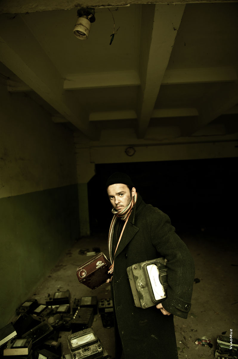 Жанровый портрет мужика в черном пальто и шапке с электроаппаратами в руках