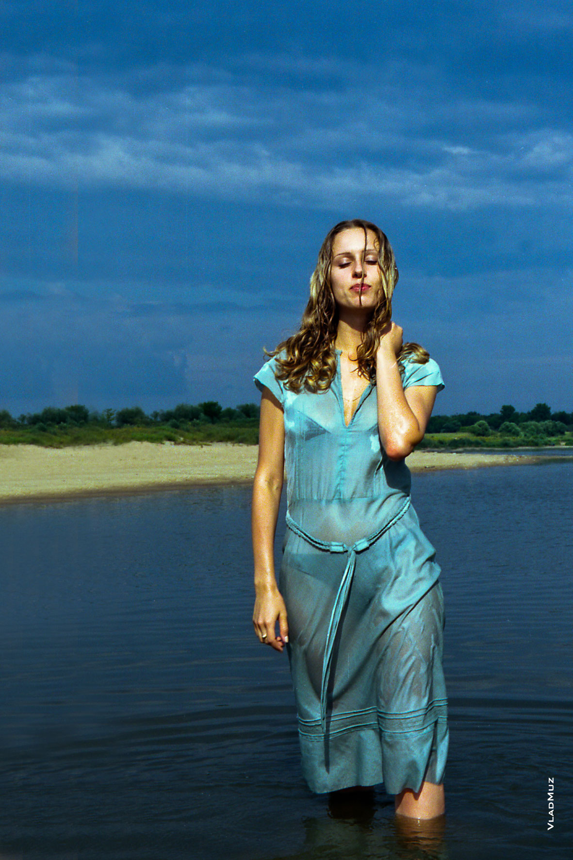 Фото девушки в полный рост, стоящей в воде, на фоне реки и синего неба