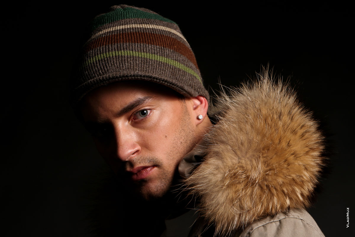 Горизонтальный студийный фотопортрет мужчины в полоборота в шапке и зимней куртке