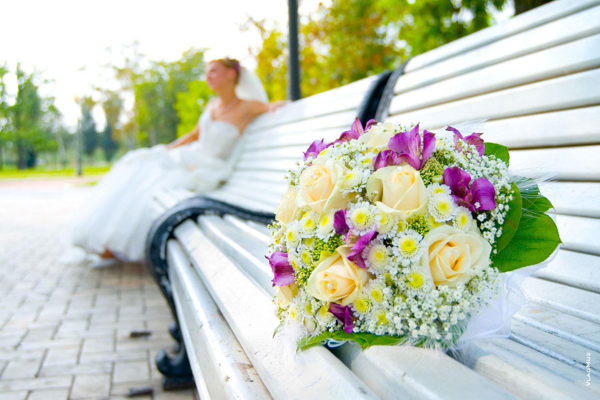 Фотография про букет невесты: букет на лавочке в фокусе, невеста вдали в расфокусе