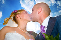 Фото поцелуя жениха и невесты на фоне синего неба в контровом солнечном свете