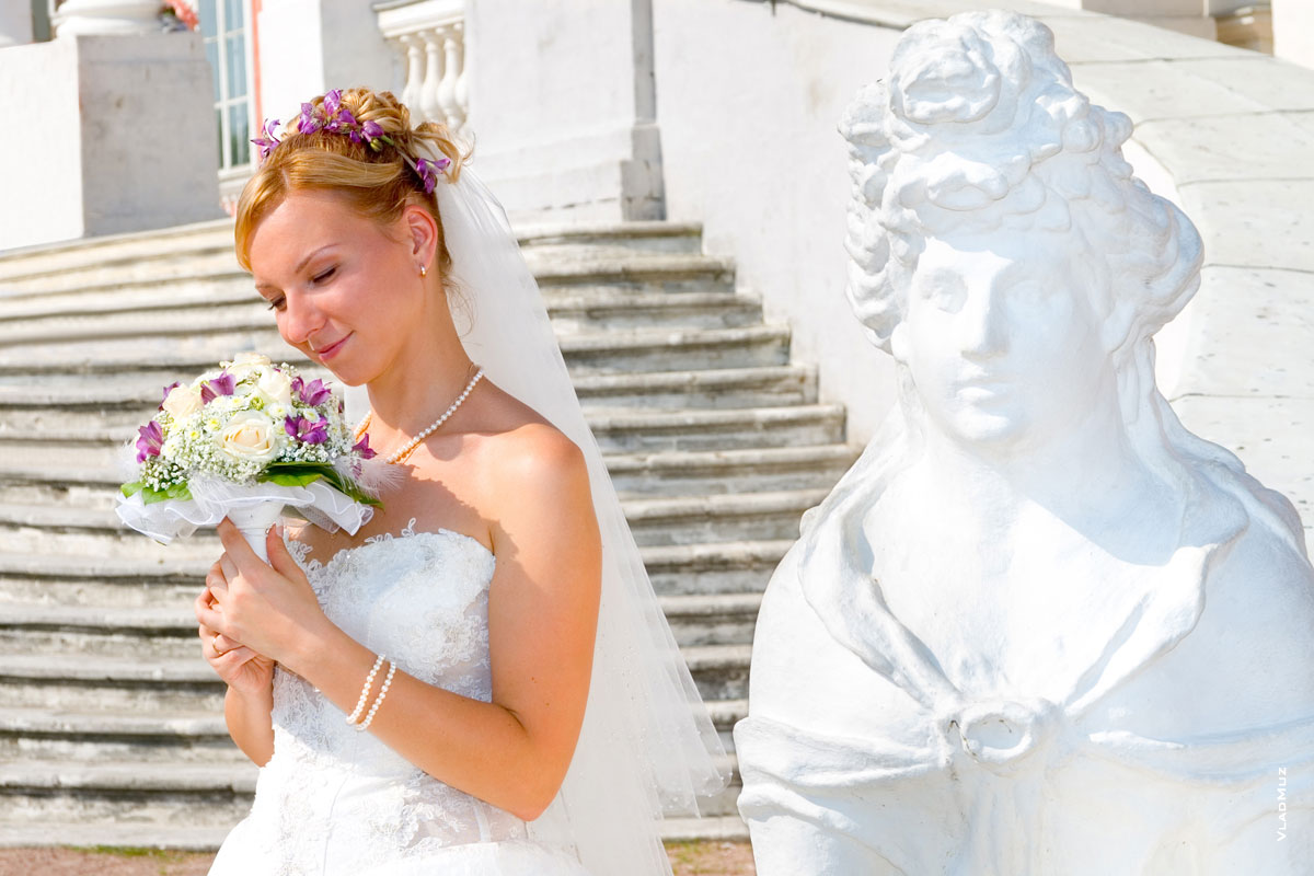 Фото невесты с букетом рядом с женской фигурой сфинкса у парадного входа в дворец усадьбы Кусково