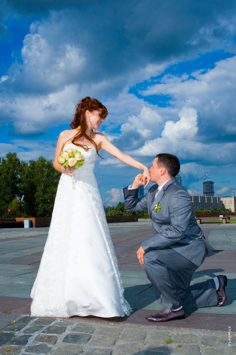 Жених целует невесте руки на фоне яркого синего неба