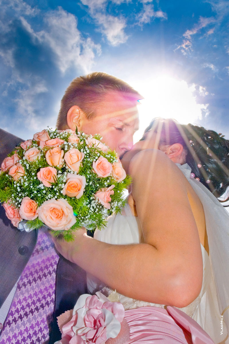 Фото свадебного поцелуя новобрачных на фоне неба в контровом солнечном свете